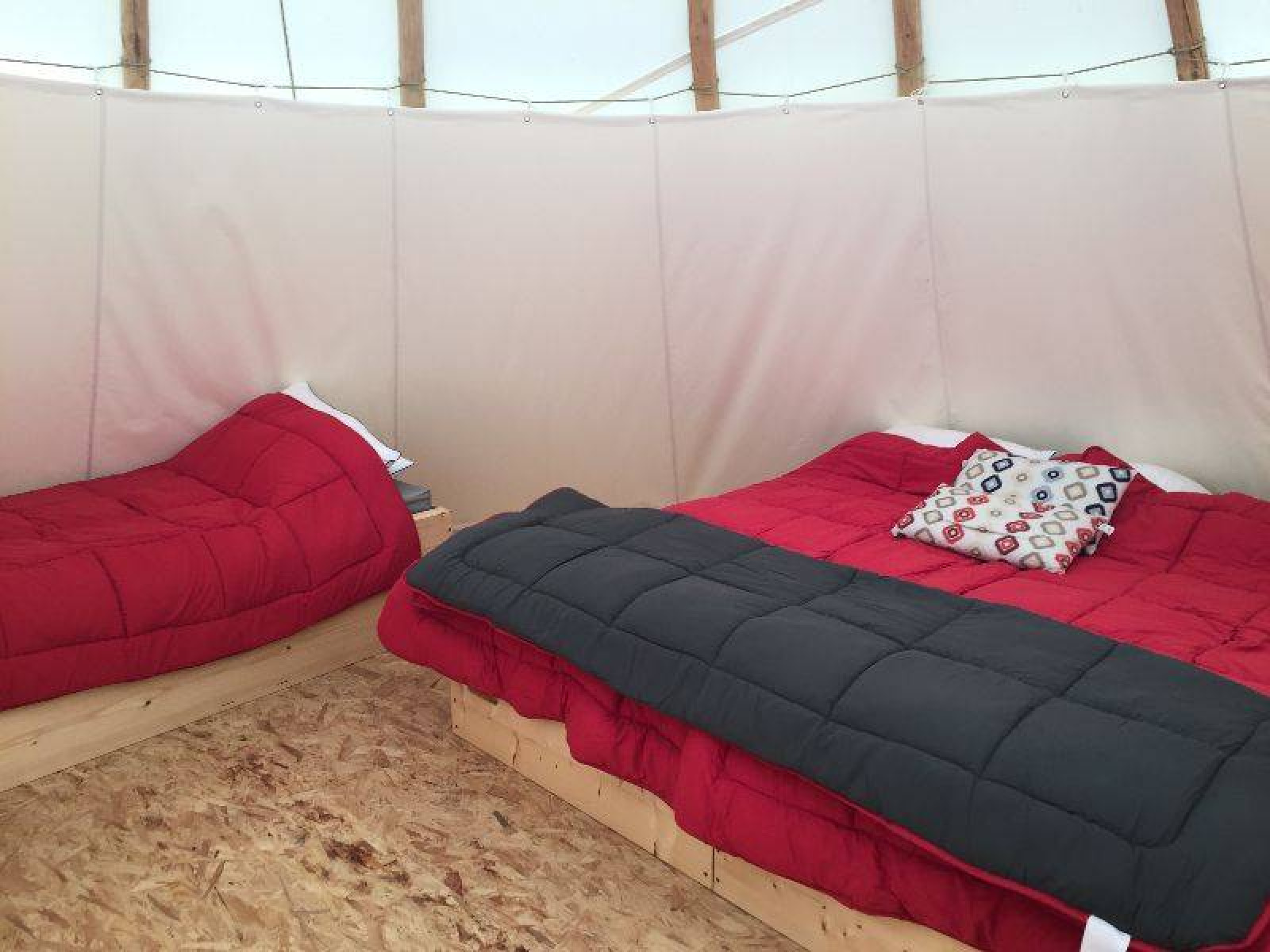 Binnenkant van een tipi tent met twee bedden en rood beddengoed bij Camping les Rives de Grand Lieu in Frankrijk.