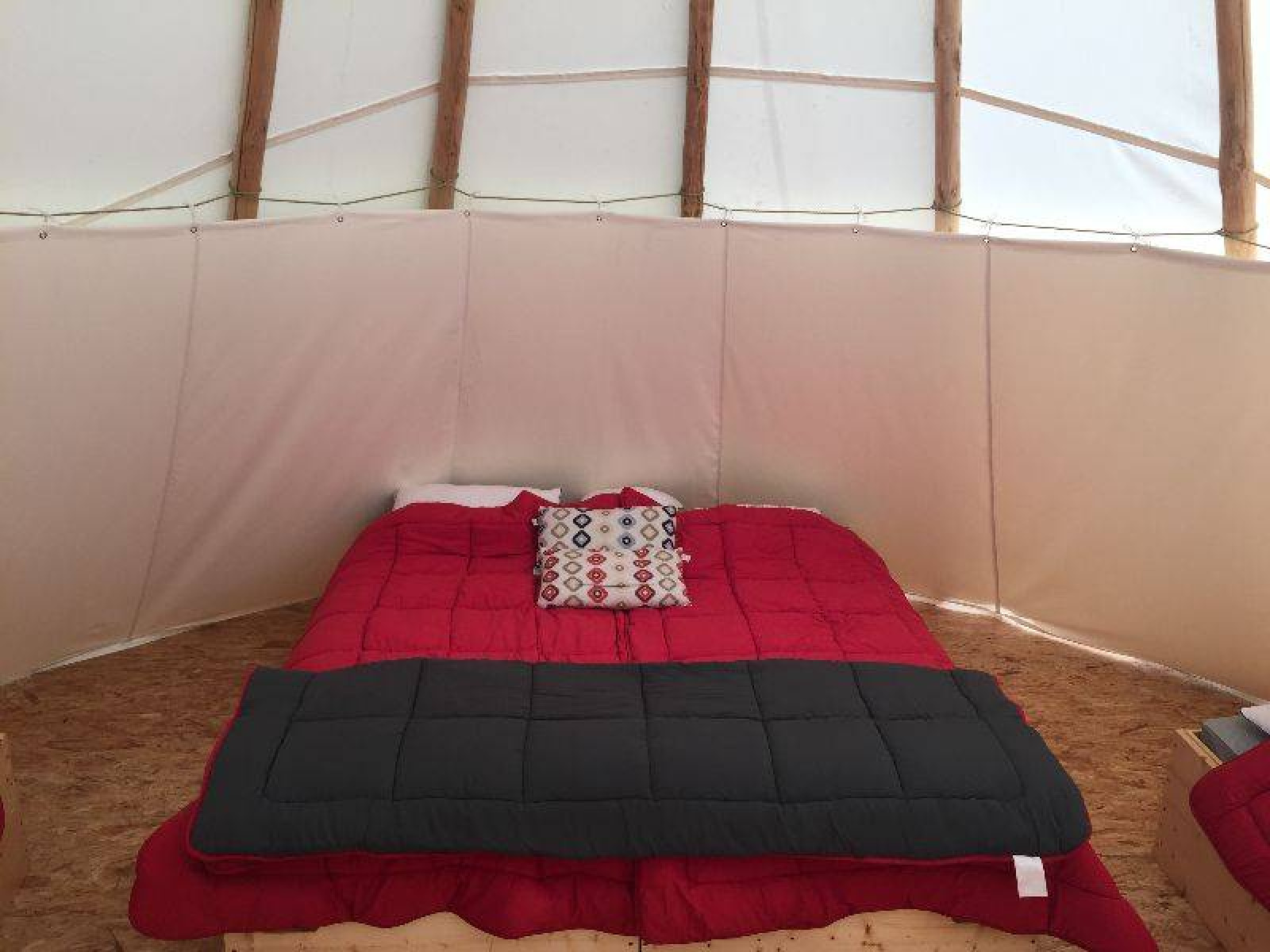 Interieur van een tipitent met rood bed en sierkussen bij Camping les Rives de Grand Lieu in Frankrijk.