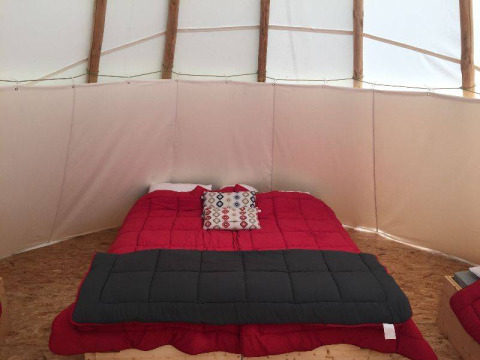 Interno di una tenda tipi con letto rosso e cuscino decorativo a Camping les Rives de Grand Lieu in Francia.