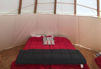 Interno di una tenda tipi con letto rosso e cuscino decorativo a Camping les Rives de Grand Lieu in Francia.