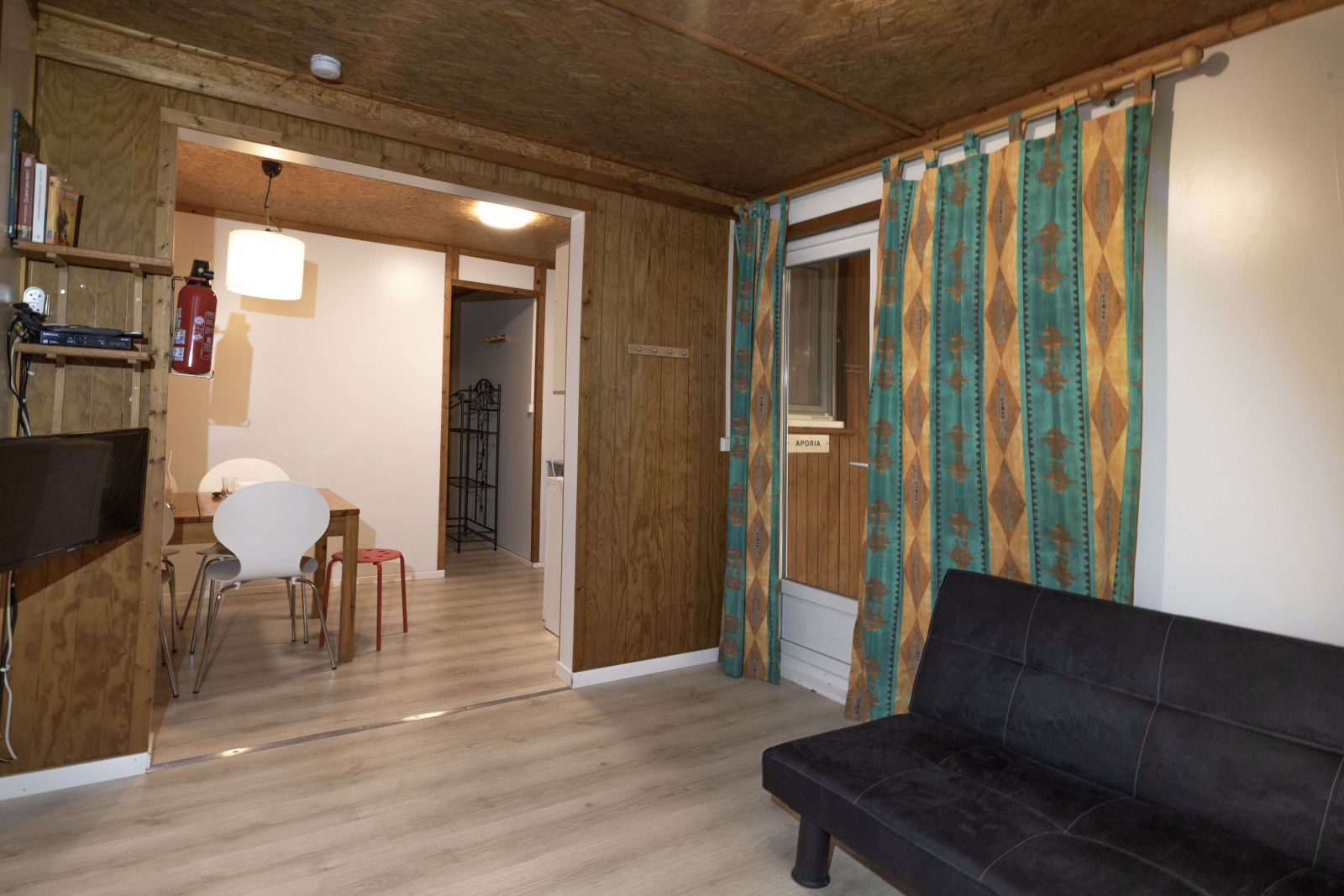 Woonkamer in Cottage Aporia bij Domaine Papillon, Frankrijk, met zwarte slaapbank en kleurrijke gordijnen.