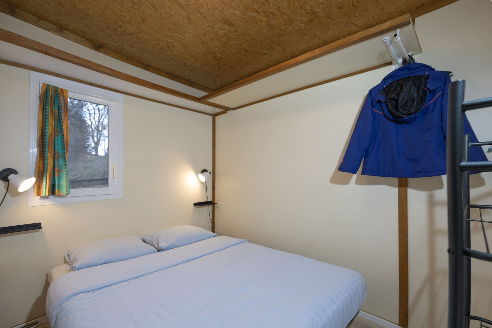 Slaapkamer in Cottage Aporia bij Domaine Papillon in Frankrijk met tweepersoonsbed en blauwe jas.