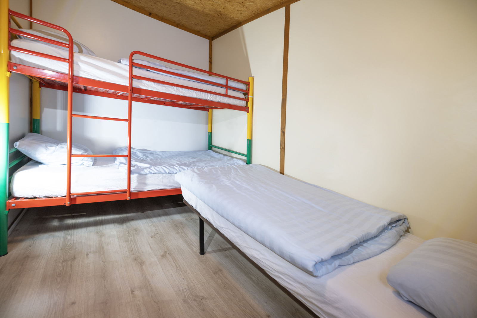 Kamer met stapelbed en eenpersoonsbed in Cottage Aporia, Domaine Papillon, Frankrijk. Houten vloer, lichte muren.