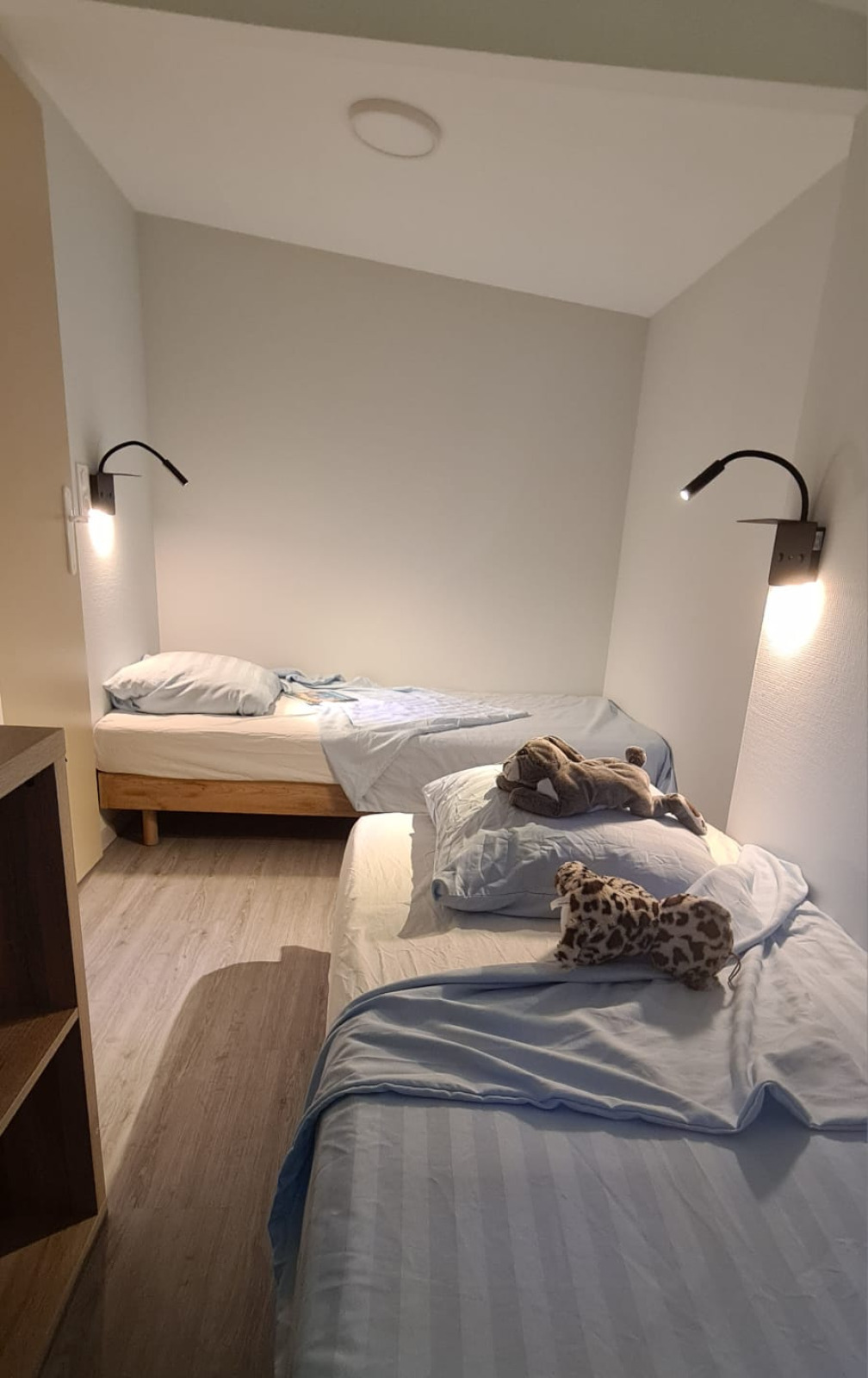 Twee eenpersoonsbedden met blauw beddengoed en wandlampen in een knusse kamer van Chalet Etoilé.