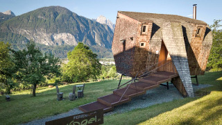 Das einzigartige Naturhaus Ufogel mit Panoramablick auf die Berge, rustikaler Holzbauweise und grüner Wiese.