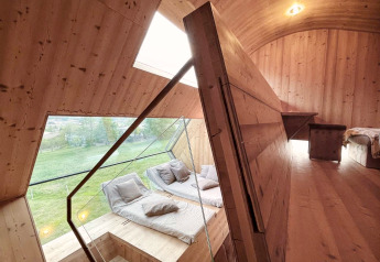 Innenraum des Ufogel-Naturhauses in Österreich mit Holzdesign, großen Fenstern und gemütlicher Sitzecke.