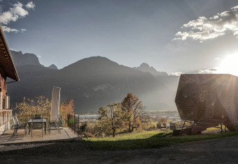 Sonnenuntergang hinter Bergen, traditionelles Holzhaus und Ufogel-Naturhaus in Österreich mit Terrasse.