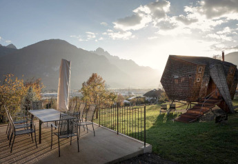 Blick auf das Naturhaus Ufogel in Österreich bei Sonnenuntergang mit Berglandschaft und Terrasse.
