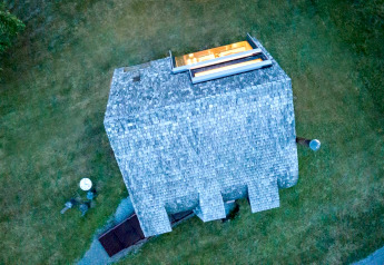 Luftaufnahme des Ufogel-Naturhauses in Österreich mit besonderem Dach und beleuchtetem Innenraum.