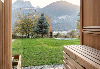 Blick aus der Sauna im Ufogel-Naturhaus in Österreich mit Bergen und grünem Garten durch ein großes Fenster.