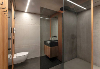 Modernes Badezimmer im Ufogel Nature House in Österreich mit Betonwänden, Glasdusche und Wandtoilette.
