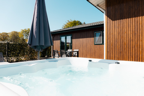 Bain à remous extérieur et terrasse avec mobilier de jardin et parasol au Wilbrinkchalet, entouré de verdure.