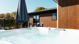 Udendørs spa og terrasse med havemøbler og paraply ved Wilbrinkchalet, omgivet af grønne træer.