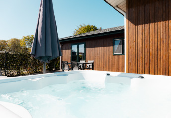 Außen-Whirlpool und Terrasse mit Gartenmöbeln und Sonnenschirm bei Wilbrinkchalet im Grünen.