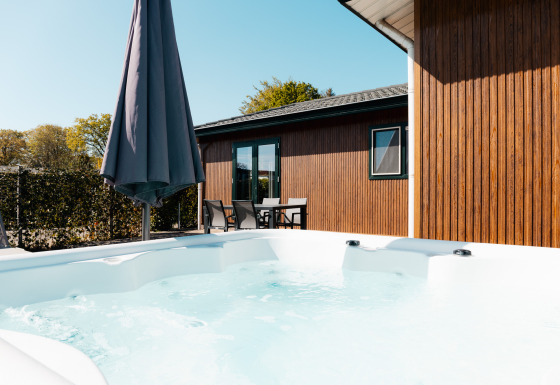 Jacuzzi exterior y terraza con muebles de jardín y sombrilla en Wilbrinkchalet, rodeado de vegetación.