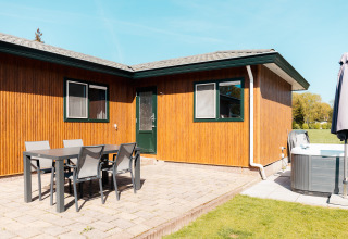 Buitenpatio bij Wilbrinkchalet op Recreatiepark De Boshoek, Nederland, met eettafel, stoelen en jacuzzi op tegels.