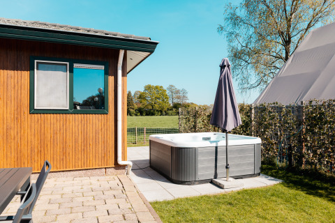 Zona exterior en el Wilbrinkchalet con jacuzzi, sombrilla y vista al campo en De Boshoek, Países Bajos.