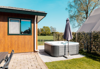 Outdoor area at Wilbrinkchalet featuring a hot tub, umbrella, and field view at De Boshoek Recreation Park, Netherlands.