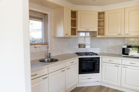 Modern kitchen with white cabinets, gas stove, built-in oven, microwave, and window in Wilbrinkchalet.