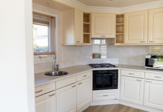 Cocina moderna con gabinetes blancos, estufa de gas, horno empotrado, microondas y ventana en Wilbrinkchalet.