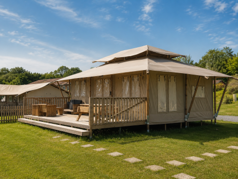 Tente safari Stardust 40 Family Lodge avec terrasse en bois et mobilier extérieur dans un cadre verdoyant.