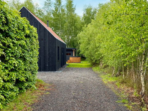Lodge in legno nero su sentiero ghiaioso, circondato da alberi verdi a Forest villa «De Bosburcht», De Kremmer, Paesi Bassi.