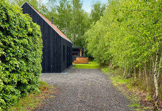 Zwart houten lodge aan een grindpad, omringd door groene bomen bij Forest villa «De Bosburcht» in De Kremmer, Nederland.