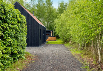 Zwart houten lodge aan een grindpad, omringd door groene bomen bij Forest villa «De Bosburcht» in De Kremmer, Nederland.
