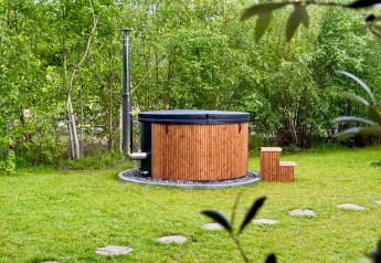 Holzverkleideter Außen-Whirlpool mit Schornstein im Garten, umgeben von Bäumen bei einer Lodge.