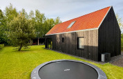 Modern black wood forest villa with red roof, built-in garden trampoline, lush grass and surrounding trees.
