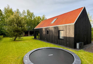 Casa in legno nera dal tetto rosso, giardino verde con trampolino interrato, alberi tutt'intorno.