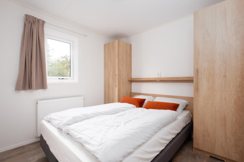 Soveværelse med dobbeltseng, hvidt sengetøj, orange puder og træskabe i Bungalette comfort hos Mölke.
