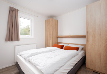 Chambre avec lit double, linge blanc, coussins orange et armoires en bois au Bungalette Comfort à Mölke.