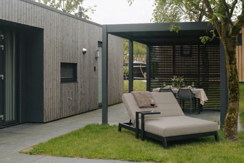 Área de descanso exterior en Oak Lodge con tumbona, mesa de comedor y fachada de madera moderna.