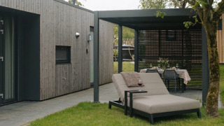Udendørs loungeområde ved Oak Lodge med solstol, spisebord og moderne træbeklædt bygning.
