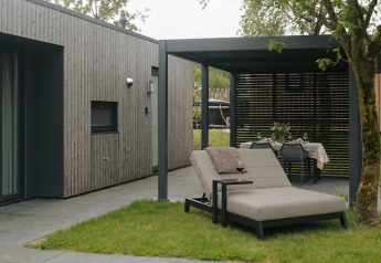 Área de descanso exterior en Oak Lodge con tumbona, mesa de comedor y fachada de madera moderna.