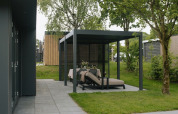 Moderne udendørs siddeplads under pergola ved Oak Lodge, Holiday park Hölte, Holland, omgivet af træer.