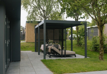 Moderne udendørs siddeplads under pergola ved Oak Lodge, Holiday park Hölte, Holland, omgivet af træer.