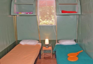 Interieur van safari tent Ecotent Lodge met twee enkele bedden en venster bij Camping Paradis Family des Issoux.