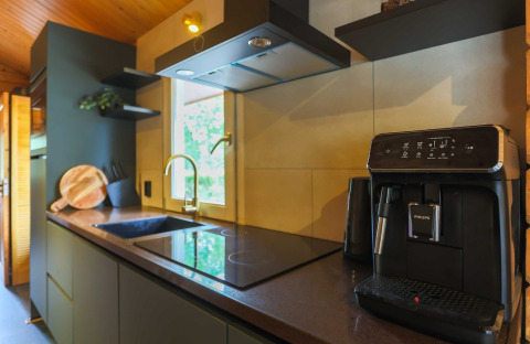 Moderne lodgekeuken met koffiemachine, inductiekookplaat, spoelbak, snijplank en raam met uitzicht.