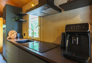 Moderne lodgekeuken met koffiemachine, inductiekookplaat, spoelbak, snijplank en raam met uitzicht.