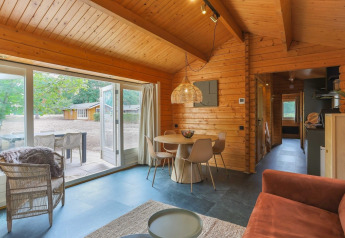 Interior view of a cozy wooden lodge with dining area, open doors, and a patio overlooking the outdoors.