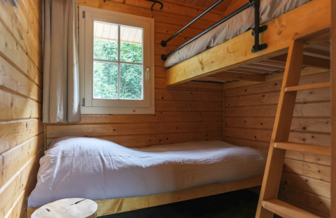 Knusse lodgekamer met houten wanden, stapelbedden, wit beddengoed en raam met zicht op bos.