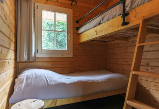 Knusse lodgekamer met houten wanden, stapelbedden, wit beddengoed en raam met zicht op bos.