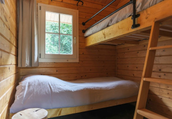 Cozy lodge room with wooden walls, bunk beds, a window with forest views, and simple white bedding.