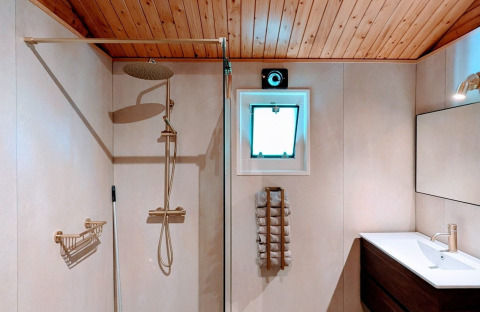 Moderne lodgebadkamer met regendouche, houten plafond, raam, handdoekenrek en modern lavabomeubel.
