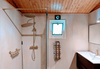 Modern lodge bathroom with a rain shower, wooden ceiling, small window, towel rack, and sleek sink.