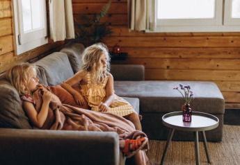 Two children sit on a cozy sofa in the Dog-friendly Swedish Village Cottage at Camping De Kleine Wereld, Netherlands.