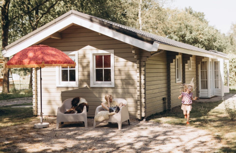Twee kinderen spelen voor een gezellige lodge met stoelen en een grote rode parasol in de tuin.