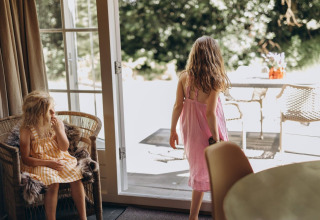Twee meisjes in zomerkleedjes ontspannen en spelen in de Zweedse lodge bij Camping De Kleine Wereld, Nederland.